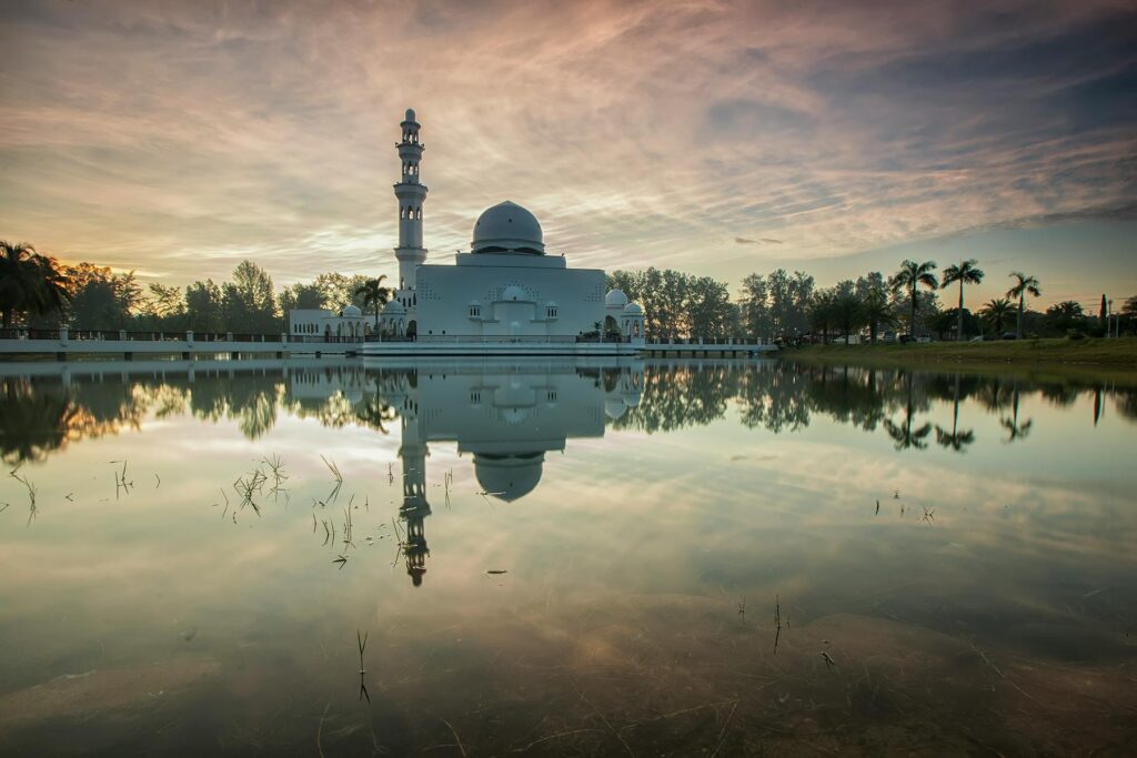 Peaceful view of a mosque reflecting in the calm waters at sunset, creating a serene landscape in Malaysia.